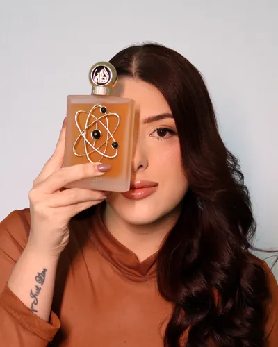 Aninha segurando um perfume árabe dourado na frente do rosto